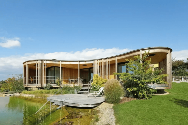 Bungalow mit Flachdach, überdachtem Terrassenbereich, bodentiefen Fenstern, Holzfassade und Schwimmteich mit Steg und Zugang von Weissenseer Holz-System-Bau.