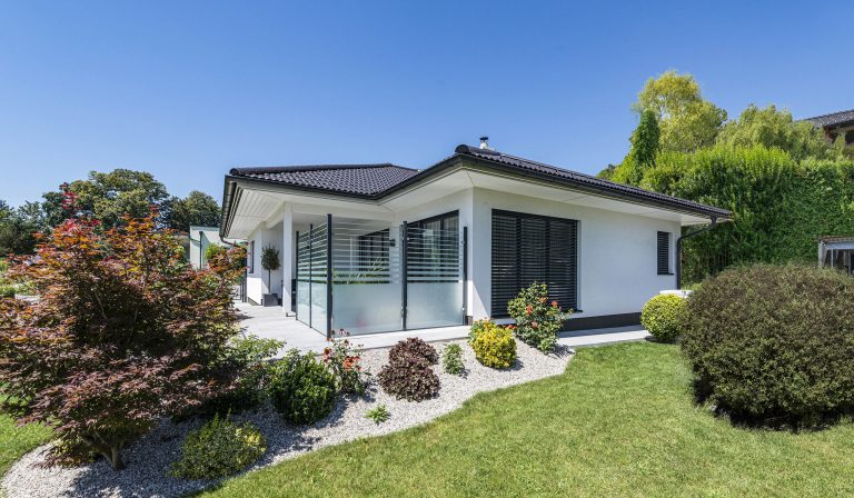 Wolf Systembau zeigt Bungalow mit Walmdach und Glaselemente als Wind- und Sichtschutz auf der Terrasse.