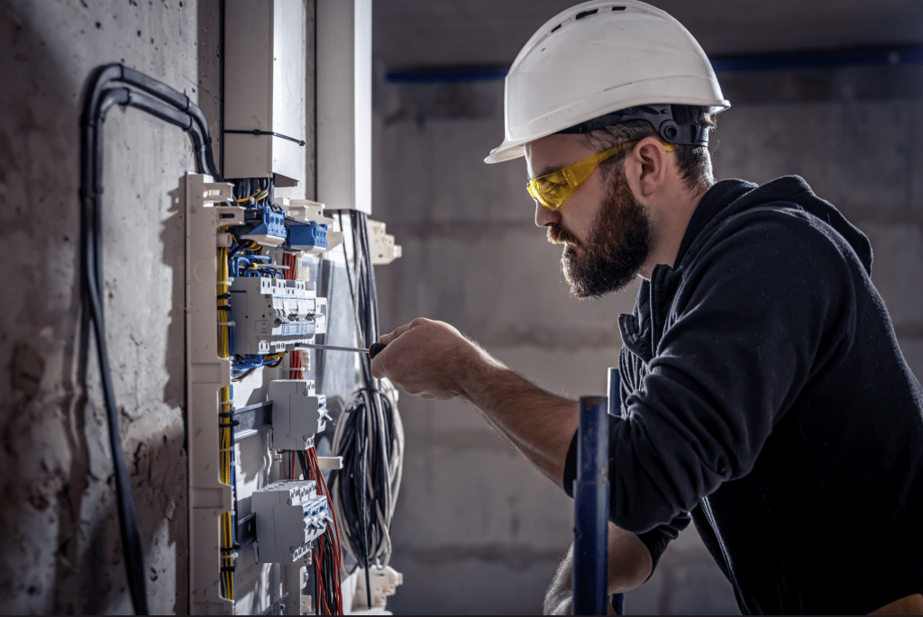 Elektriker arbeitet in einer Schalttafel mit einem Schraubenzieher an einem elektrischen Verbindungskabel und führt Elektroinstallationen aus.