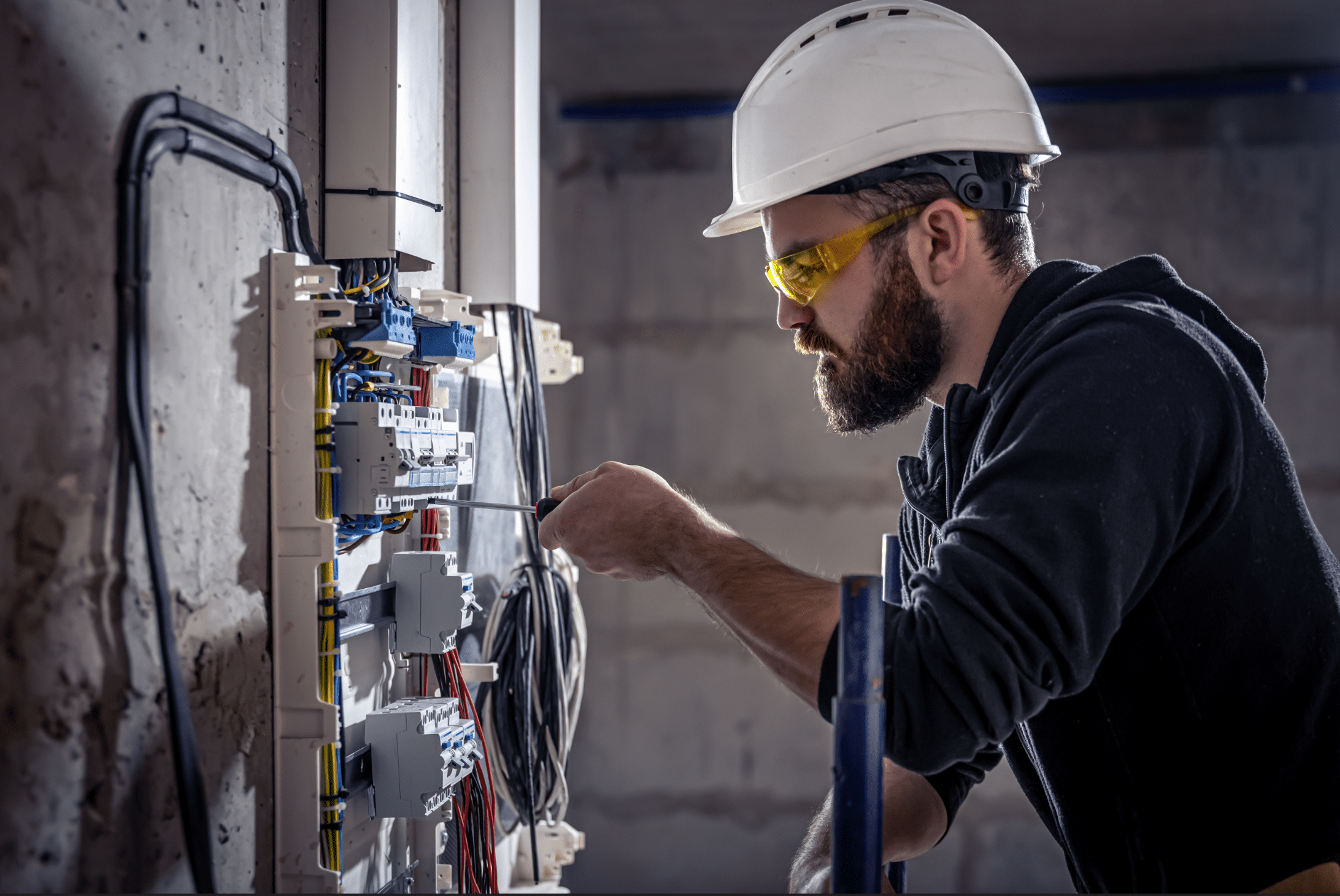 Elektriker arbeitet in einer Schalttafel mit einem Schraubenzieher an einem elektrischen Verbindungskabel und führt Elektroinstallationen aus.