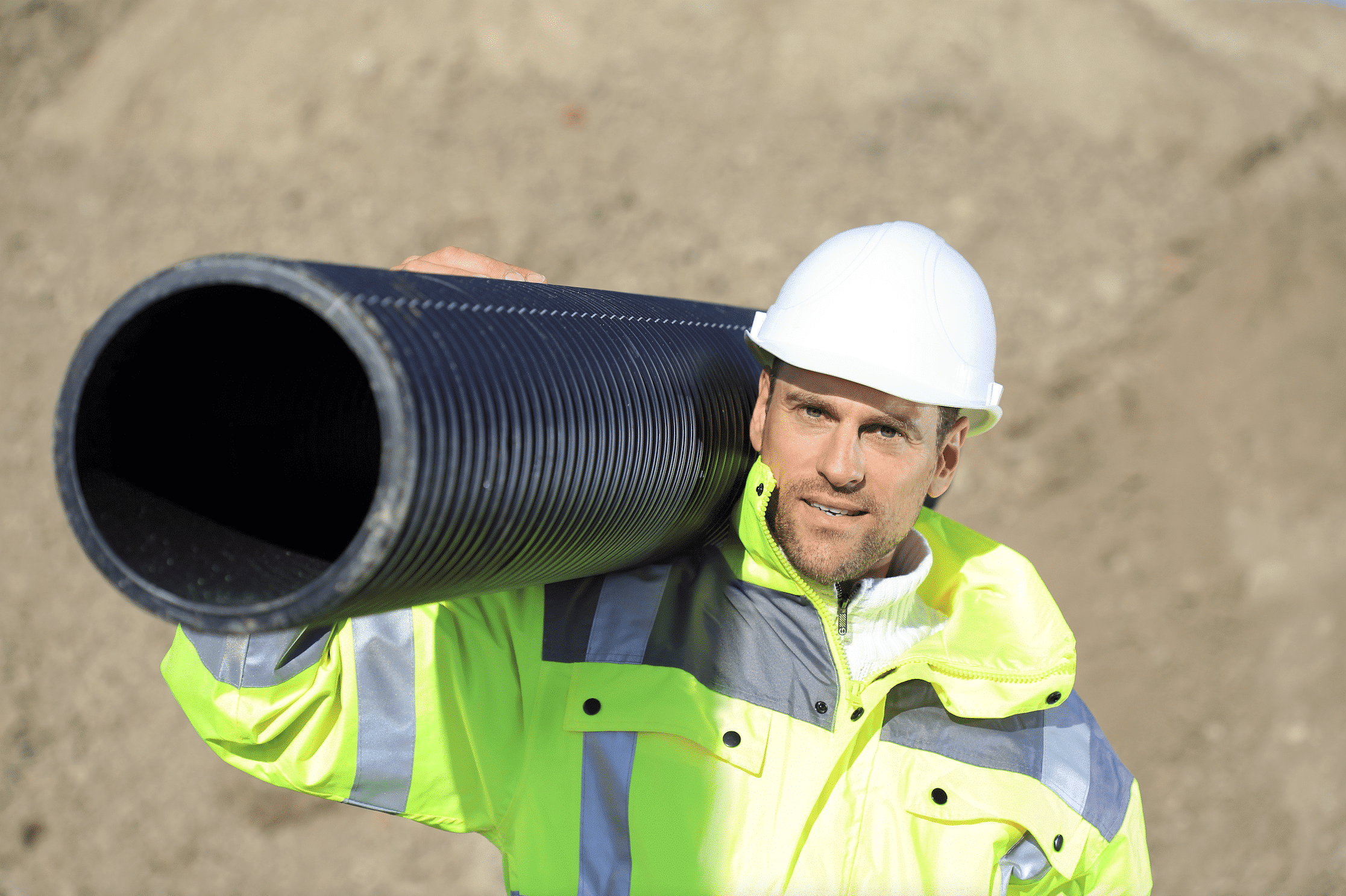 Bauarbeiter auf Baustelle trägt ein schwarzes Rohr.